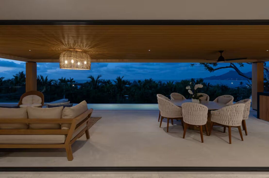 An open-plan living area with a sofa and dining table, a hanging light fixture, and a view of the outdoors.
