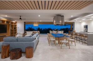Ein modernes Wohnzimmer mit einer Couch, Esstisch, Stühlen, einer Küchenzeile und einem großen Fernseher.