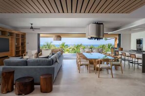 Ein modernes Wohnzimmer mit einer Couch, einem Esstisch und Stühlen, einer Küchenzeile und Blick aufs Meer.