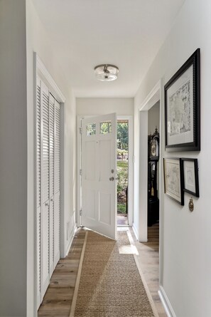 A hallway with a wooden floor, white walls, a white door, and a ceiling light fixture.
