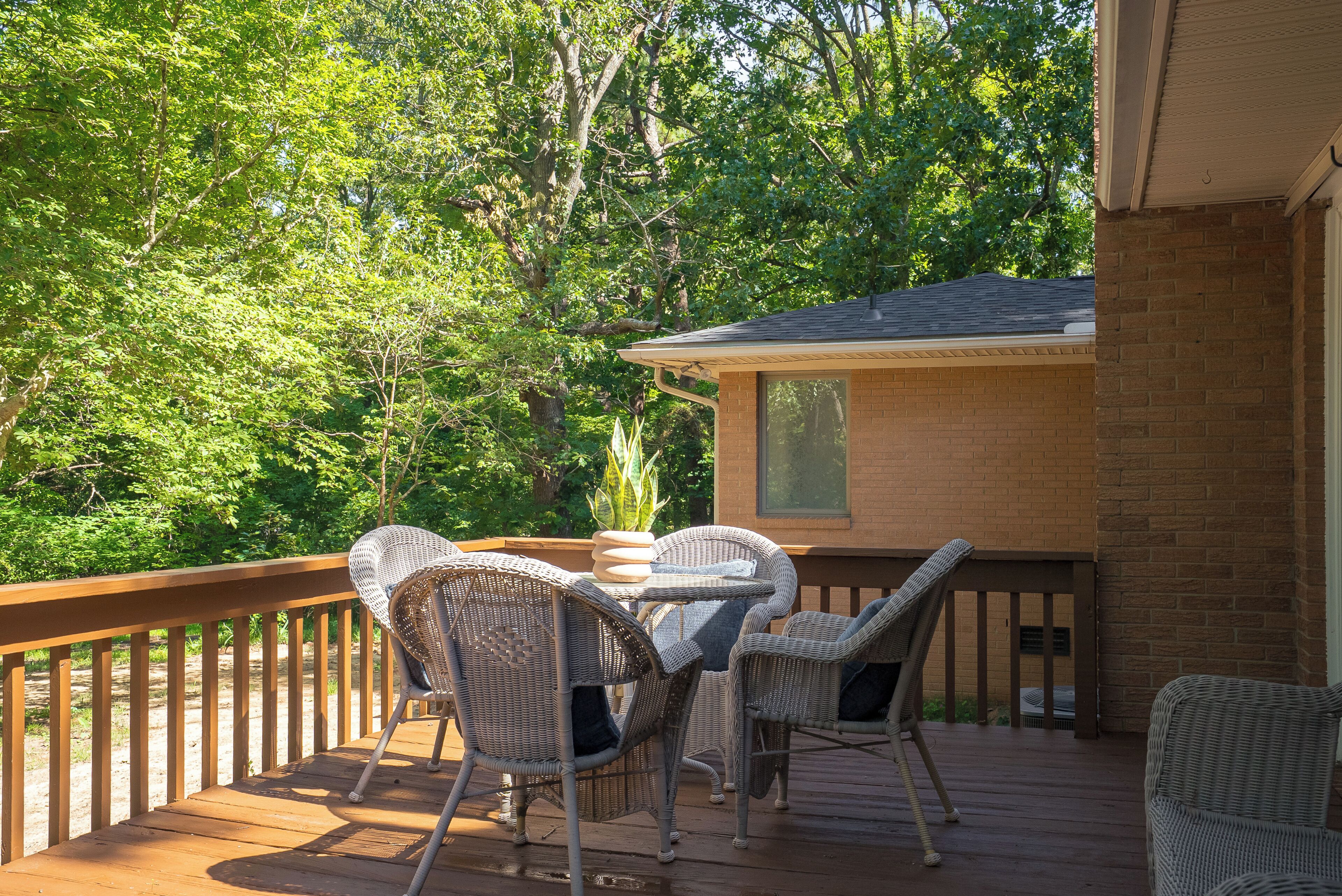 Une terrasse en bois avec des meubles en osier, un bâtiment en briques en arrière-plan et une végétation luxuriante.