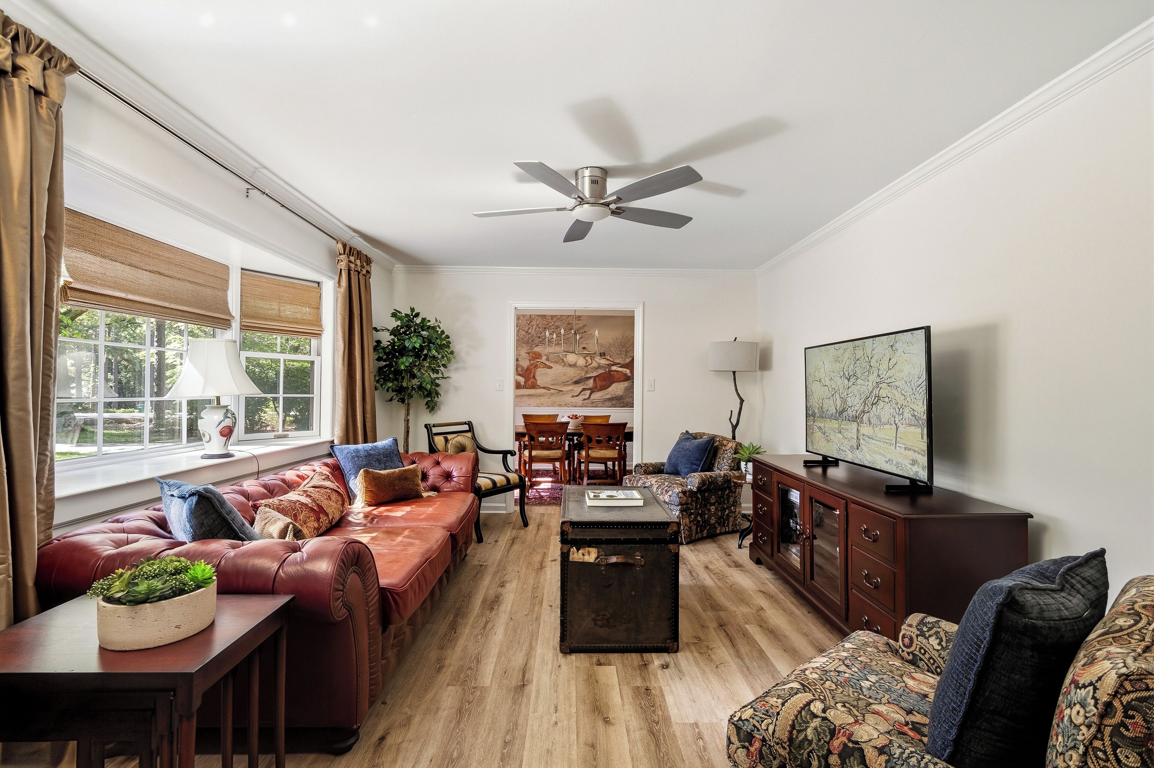 A living room with a leather sofa, a coffee table, a television, and a ceiling fan.