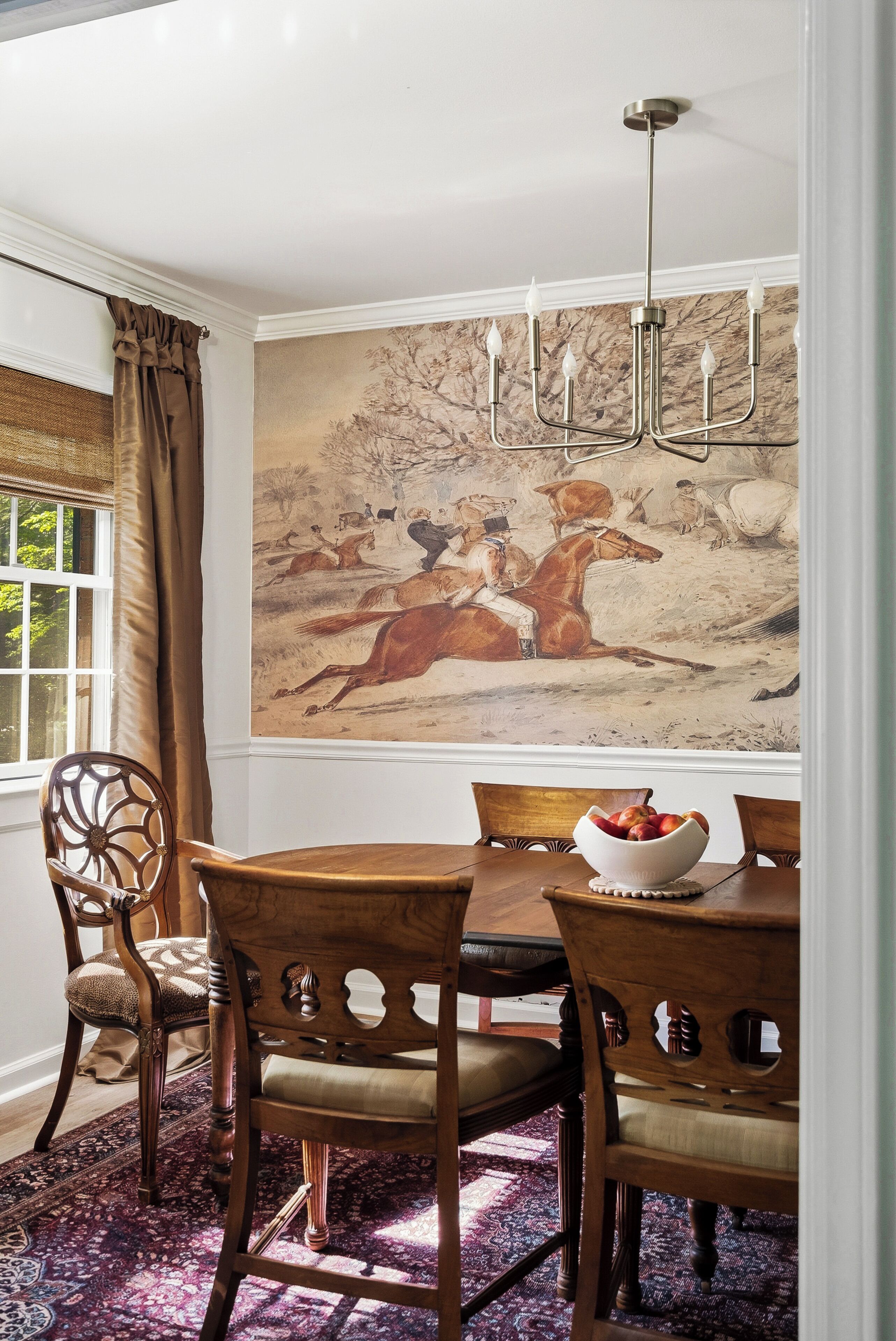 A dining room with a large painting, wooden furniture, and a chandelier.
