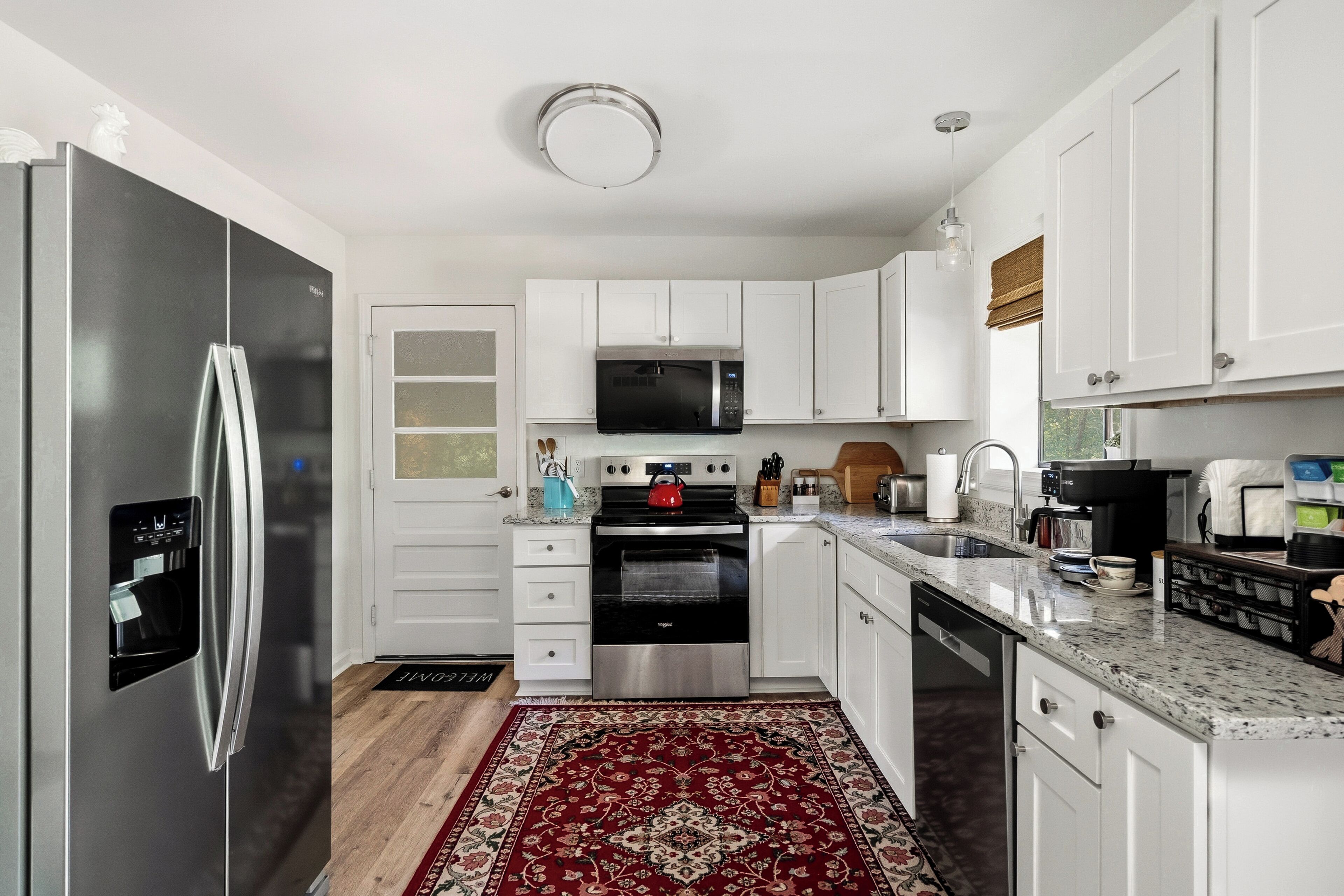 A modern kitchen with stainless steel appliances, white cabinetry, and a red patterned rug.