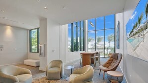 Un hall d’hôtel moderne doté d’une grande fenêtre, de sièges confortables et offrant une vue sur des palmiers.