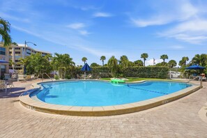 A swimming pool with a tiled deck, palm trees, and a building in the background. - *Steps to Beach|Spotless|Walkable Area|Pool* (St. Pete Beach)