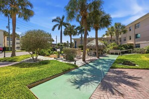 A courtyard with palm trees, a thatched-roof structure, and a green walking path. - *Steps to Beach|Spotless|Walkable Area|Pool* (St. Pete Beach)