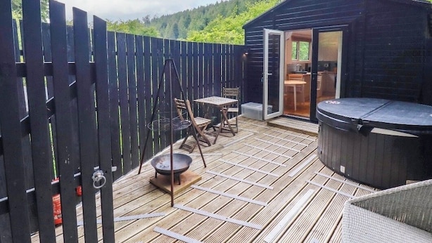 A wooden deck with a hot tub, a table with chairs, and a wooden fence.