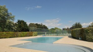 Una piscina con valla perimetral, cielo despejado y árboles al fondo.