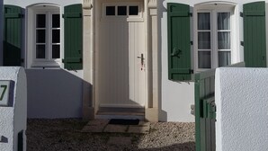 Un edificio con fachada blanca, contraventanas verdes y una puerta central con un pequeño porche.