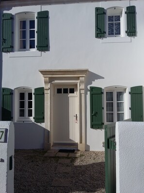 Ein Gebäude mit weißer Fassade, grünen Fensterläden und einer zentralen Tür mit kleinem Vorbau.