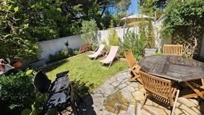 Un patio con una mesa redonda y sillas, una parrilla y dos sillones.
