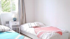 Un dormitorio con dos camas, una mesita de noche, una lámpara y una ventana con cortinas.