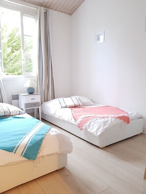 Ein Schlafzimmer mit zwei Betten, einem Nachttisch, einer Lampe und einem Fenster mit Vorhängen.