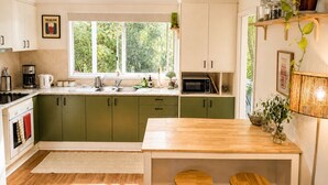 Una cocina con armarios verdes, encimera de madera, un lavabo y una ventana con vistas a la vegetación.