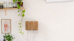 Una sala de estar con un sofá verde, una manta amarilla y un cojín a rayas. Hay una silla de mimbre y una pequeña mesa de madera.