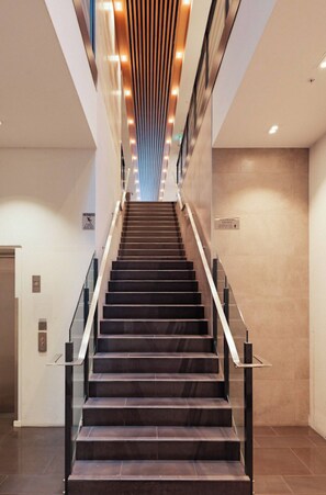Eine moderne Treppe mit dunklen Stufen und Glastrennungen, die zu einer Zwischenebene mit einer vertikalen Leuchte führt.