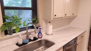 A kitchen with a sink, countertop, cabinets, and a window with plants. - Delightful 2-bedroom house in Stephenville just STEPS from Tarleton State (Stephenville)