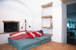 Une pièce chaleureuse avec un lit, une cheminée et un coin repas visible à travers une arche.