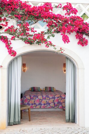 Quarto com cama, um banco e vista através de um arco.