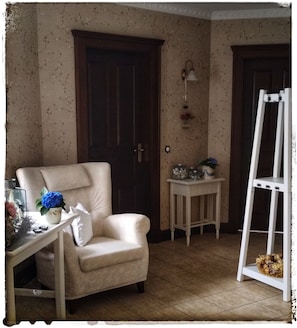 Une piÚce avec un fauteuil beige, une petite table sur laquelle est posé un vase de fleurs, une échelle blanche et deux portes.