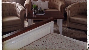 Ein Zimmer mit blumigem Wandpapier, zwei Sessel, ein Sofa, ein Couchtisch mit Pflanze und eine Pendelleuchte.