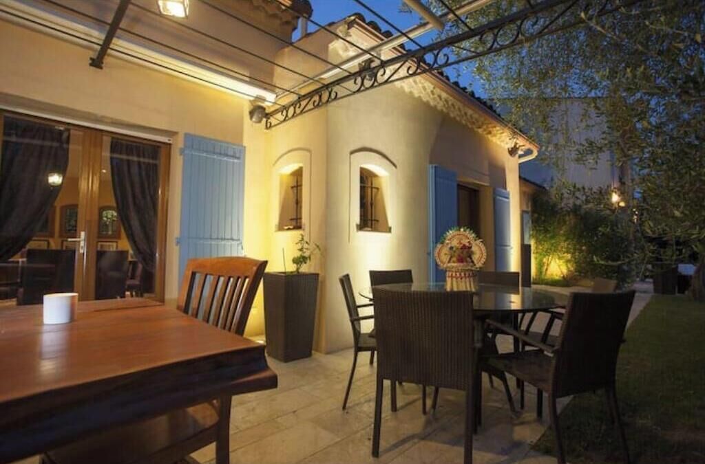 An outdoor patio area with a wooden table and chairs, a small garden, and a building with a balcony.