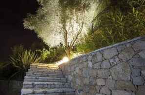 Eine Steintreppe führt zu einem Baum mit Lichtern, umgeben von viel Grün.