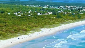 A coastal beach with a sandy shore, clear blue water, and a distant view of a residential area. - First Floor Condo on Golf Course Near Beach (Fort Pierce)