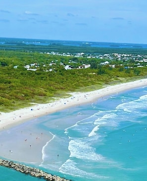Ein Küstenstrand mit sandigem Ufer, klarem, blauem Wasser und einer entfernten Ansicht eines Wohngebiets.