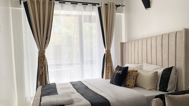 Een slaapkamer met een groot bed, een hoofdbord en een raam met gordijnen.