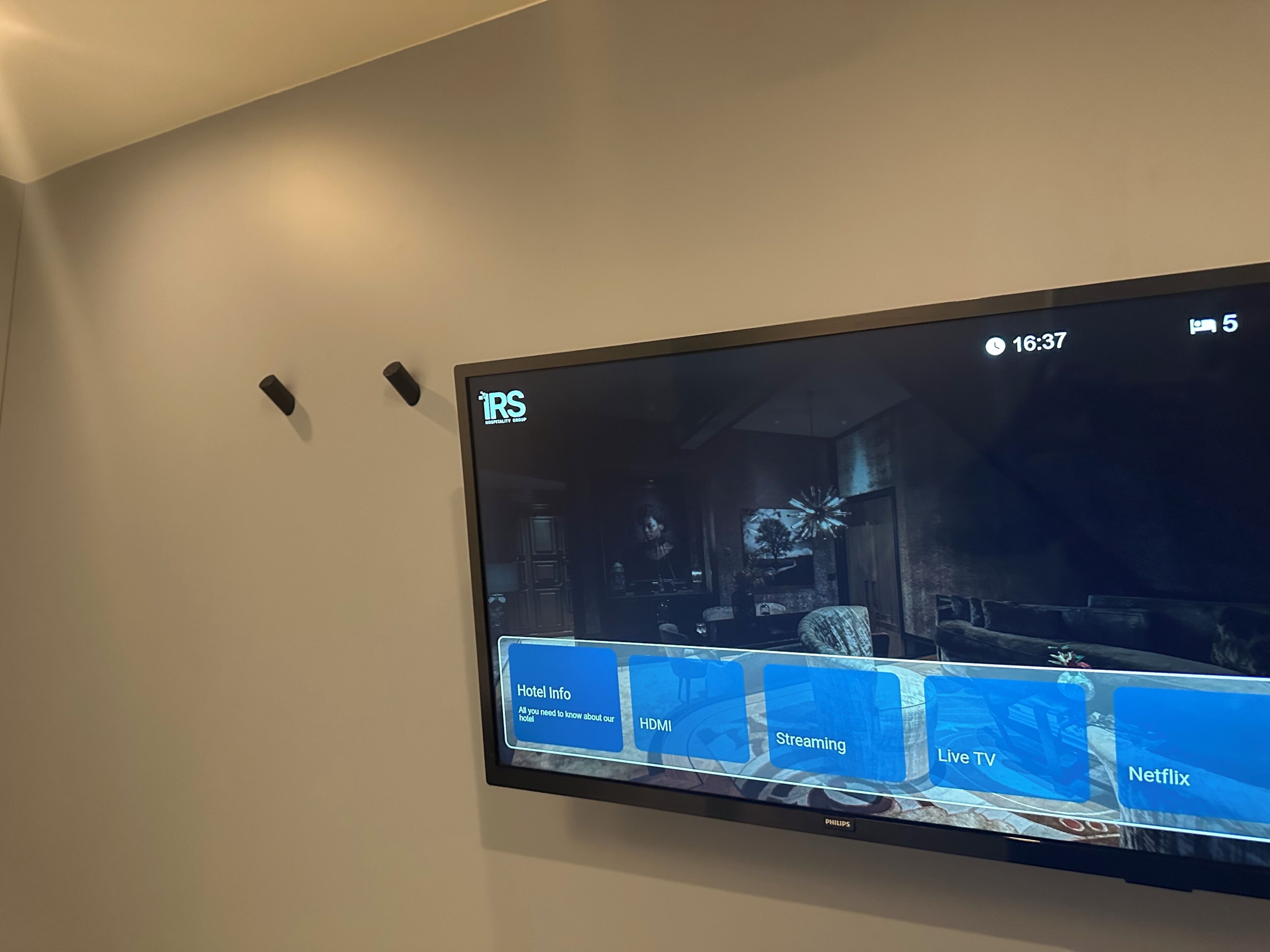 A flat-screen TV mounted on a wall displaying a hotel information interface with options for hotel info, HDMI, streaming, live TV, and Netflix.