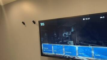 A flat-screen TV mounted on a wall displaying a hotel information interface with options for hotel info, HDMI, streaming, live TV, and Netflix.