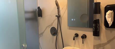 Un baño moderno con pared de mármol, ducha de mano, lavamanos, dispensador de toallas y estación de lavado de manos.