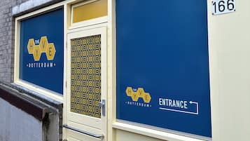 A building facade with a blue and yellow entrance sign, a door with a patterned glass panel, and a number '166' on the wall.