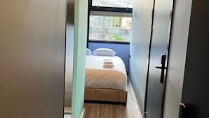 Un couloir étroit mène à une chambre à coucher qui contient un lit, une fenêtre et une porte.