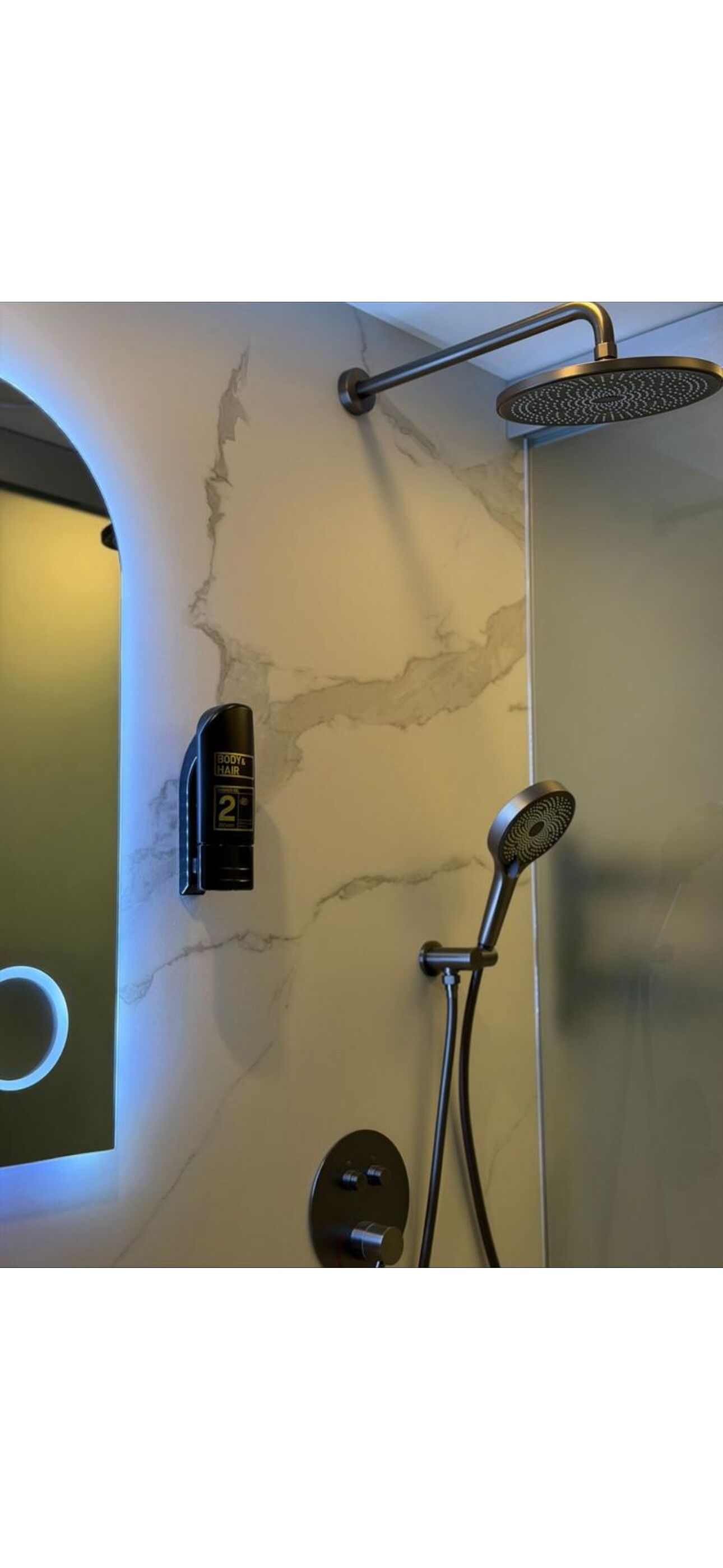 A bathroom with a marble wall, a shower with a handheld showerhead, and a wall-mounted control panel.