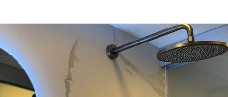 A bathroom with a marble wall, a shower with a handheld showerhead, and a wall-mounted control panel.