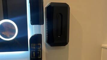 A bathroom with a hand sanitizer dispenser, a soap dispenser, a toilet paper holder, and a sink.