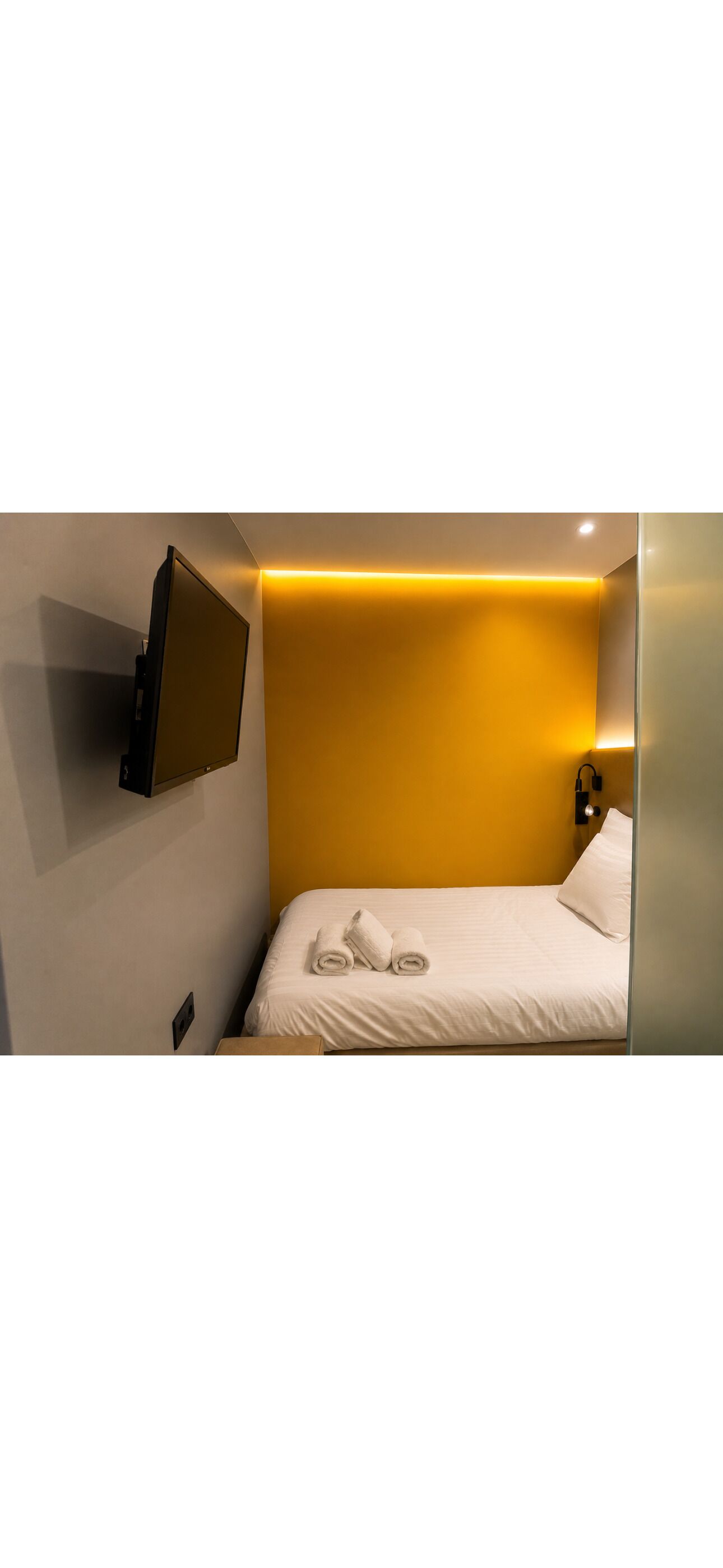 Une chambre d’hôtel avec un lit, un téléviseur à écran plat fixé au mur et une table de chevet.