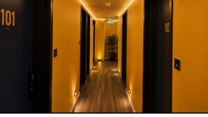 Un couloir d’hôtel avec des portes numérotées 101 et 10, une plante et une caméra de surveillance.