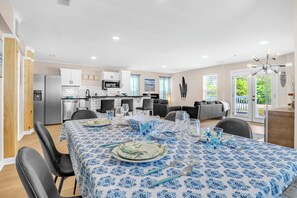 A modern kitchen with white cabinets, a stainless steel refrigerator, and a dining area with a blue patterned tablecloth.