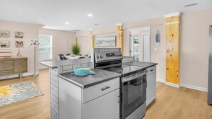A modern kitchen with a built-in oven, a dining area with a table and chairs, and a wooden door. - Stay Salty | Coastal Getaway in Surf City | Dog Friendly (Surf City)