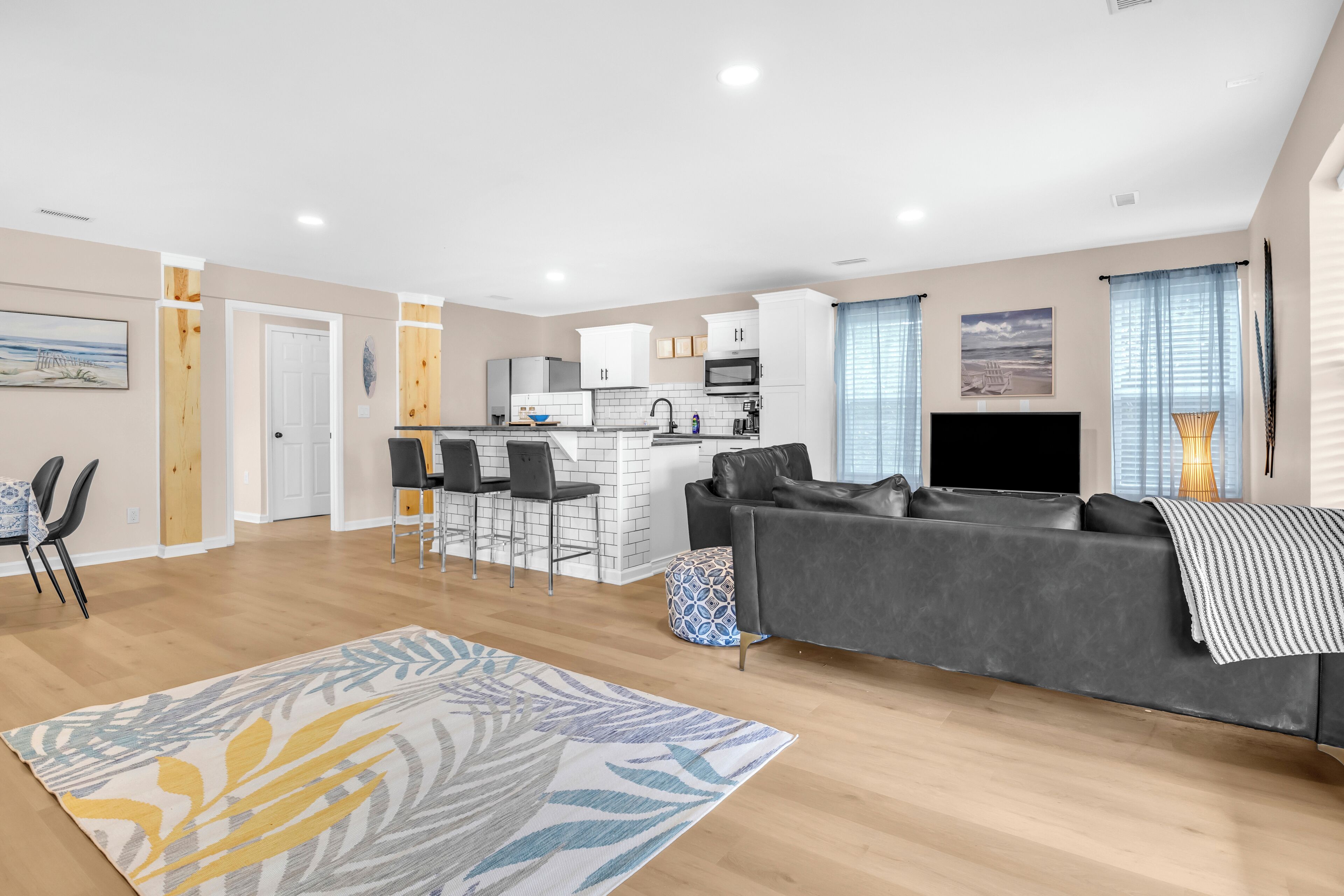 A modern living room with a grey sofa, a patterned rug, and a kitchen area with white cabinets and a microwave.