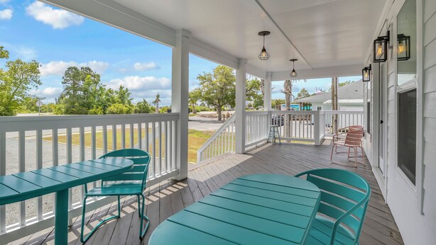 A covered porch with a white railing, teal chairs, and a table. - Stay Salty | Coastal Getaway in Surf City | Dog Friendly (Surf City)