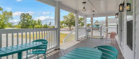 A covered porch with a white railing, teal chairs, and a table.