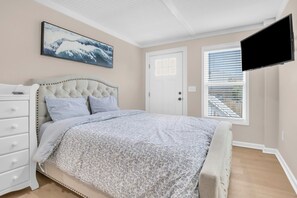 A bedroom with a bed, a dresser, a television mounted on the wall, and a window with blinds.