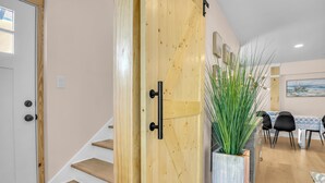 A wooden door with a black handle, a staircase, a dining area with chairs and a table, and a large potted plant. - Stay Salty | Coastal Getaway in Surf City | Dog Friendly (Surf City)