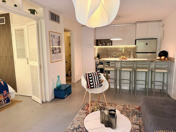 A modern kitchen with white cabinets, a central island with bar stools, and a refrigerator.