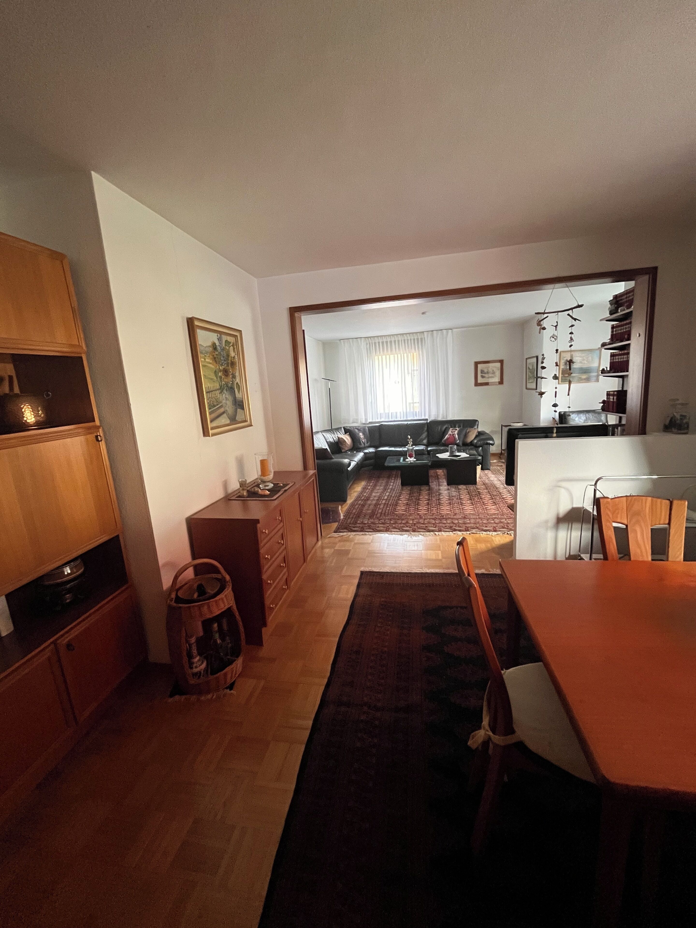 A living room with a sofa, a dining table, and a kitchen area visible through an open doorway.